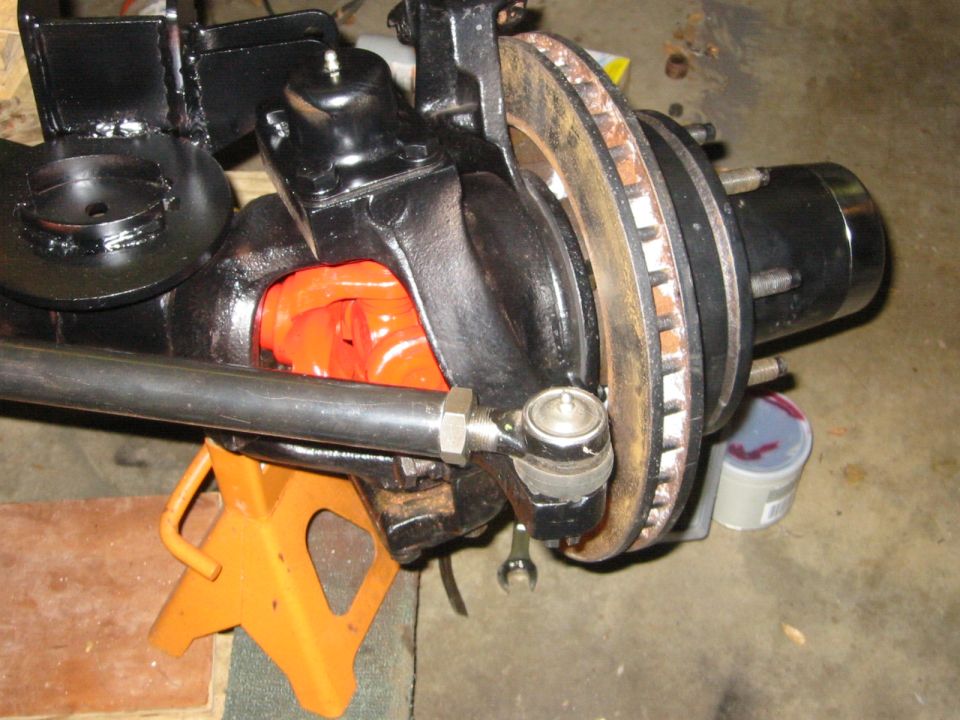 Vehicle front axle assembly with brake rotor and tie rod end, supported by an orange jack stand.
