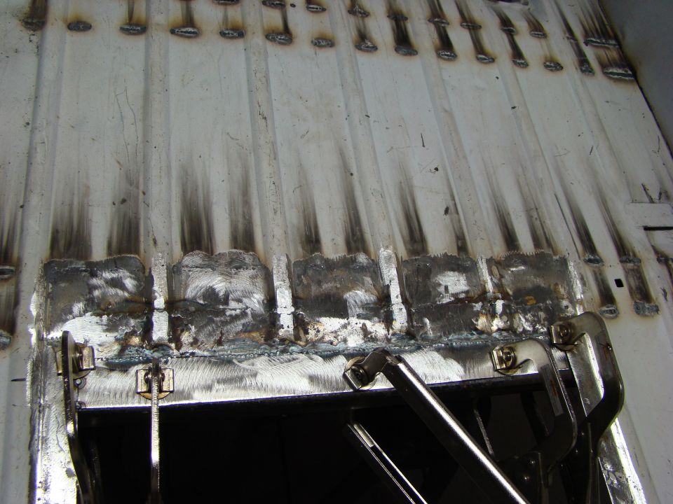 White corrugated metal surface with spot welds and grinding marks, secured by clamps.