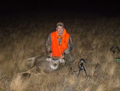 1990 Ford Bronco - A hunter kneels in a field at night, posing with a deer he has shot. A camera on a tripod is visible in the foreground.