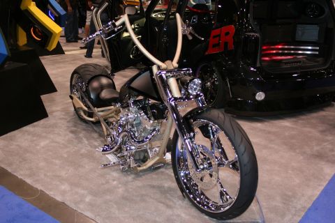 1998 Ford Crown Victoria - A custom motorcycle with extensive chrome detailing and high handlebars is displayed alongside a black SUV with red lettering on its side.