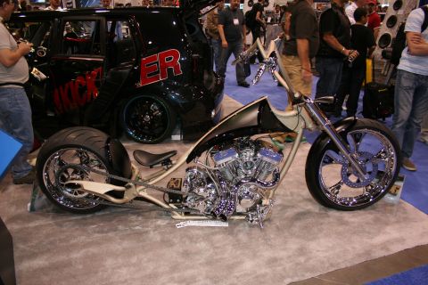 1998 Ford Crown Victoria - A custom chopper motorcycle is displayed indoors next to a black SUV with prominent red lettering.