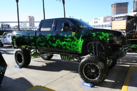1998 Ford Crown Victoria - A heavily modified black pickup truck with custom green flame graphics and large off-road tires is displayed outdoors.
