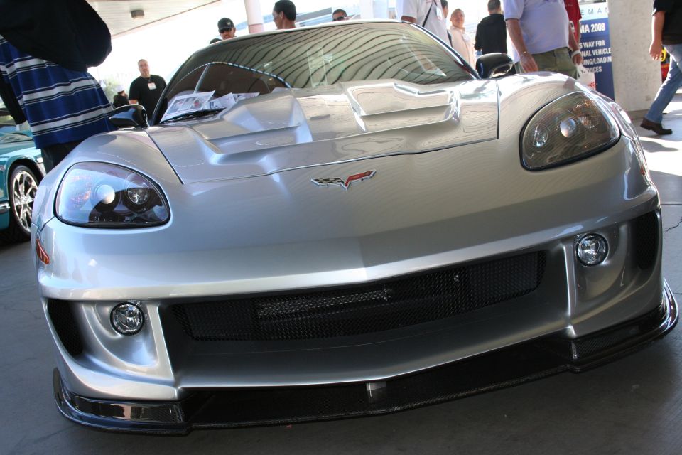 Silver sports car front view, black grille, carbon fiber splitter, people in background