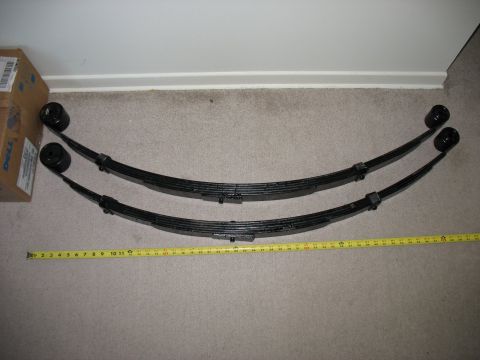 1992 Ford Bronco - Two leaf springs are laid out on a carpeted floor next to a cardboard box and a measuring tape.