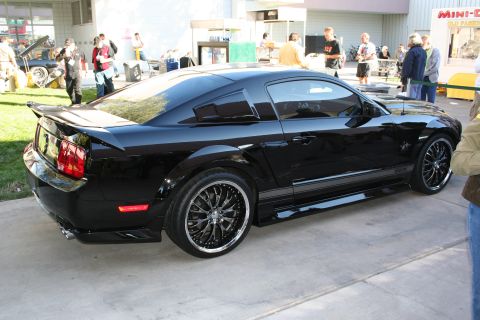 1998 Ford Crown Victoria - Black Ford Mustang with custom wheels and spoiler seen from the rear three-quarter angle.