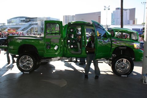 1998 Ford Crown Victoria - A heavily modified green pickup truck with custom audio equipment and large chrome wheels is displayed outdoors.