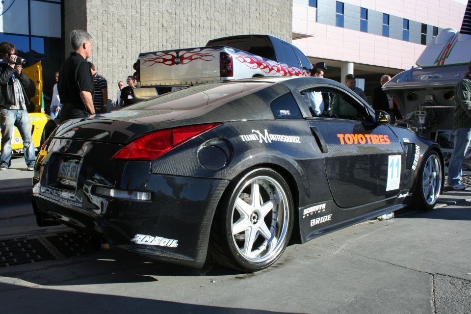 Black sports car with 'Toyo Tires' and 'Bride' decals, parked next to a pickup truck with flames