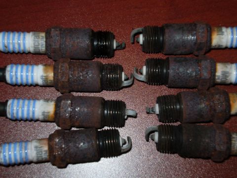1996 Ford Bronco - Eight used and rusty spark plugs are laid out on a red surface, with some text visible on the insulators.