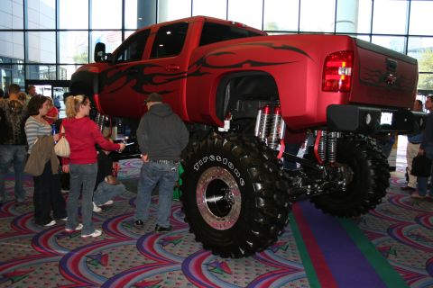 1998 Ford Crown Victoria - A heavily modified red pickup truck with custom flame decals and oversized tires is on display indoors.