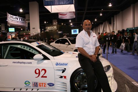 1998 Ford Crown Victoria - Man poses with a race car at an indoor event, with other vehicles and people in the background.