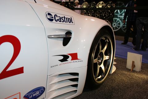 1998 Ford Crown Victoria - Close-up of a white racing car's fender and wheel, displaying sponsor decals and a large number.