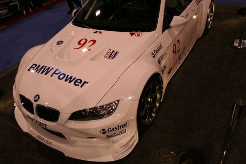 1998 Ford Crown Victoria - White BMW M3 race car with "BMW Power" livery and racing numbers is displayed indoors.
