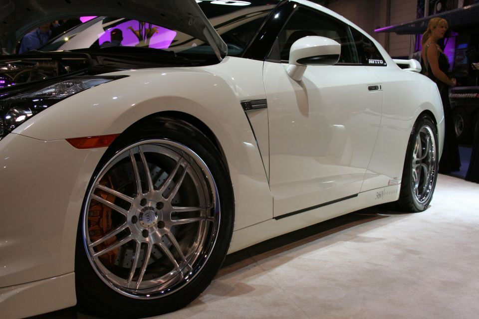 White sports car with aftermarket wheels and orange brake calipers. Hood is open showing engine components