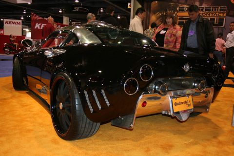 1998 Ford Crown Victoria - A custom black sports car is displayed indoors on an orange carpet, with people in the background.
