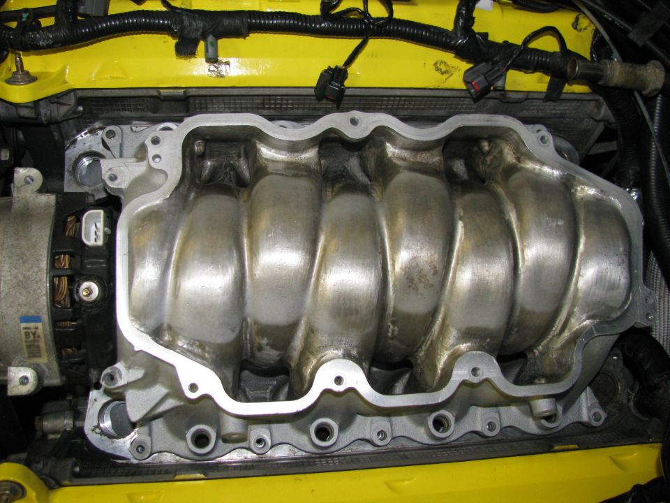 Close-up of a silver aluminum engine intake manifold with yellow engine components visible