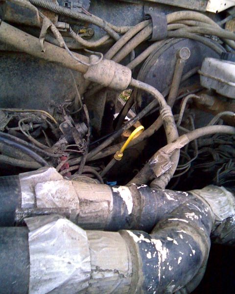 1989 Ford Bronco - Dirty engine-bay close-up dominated by large black intake or snorkel tubing wrapped with duct tape at the joints and routed across the fron…