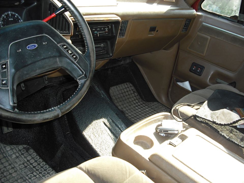 Worn tan interior of a Ford truck showing steering wheel, dash and floor
