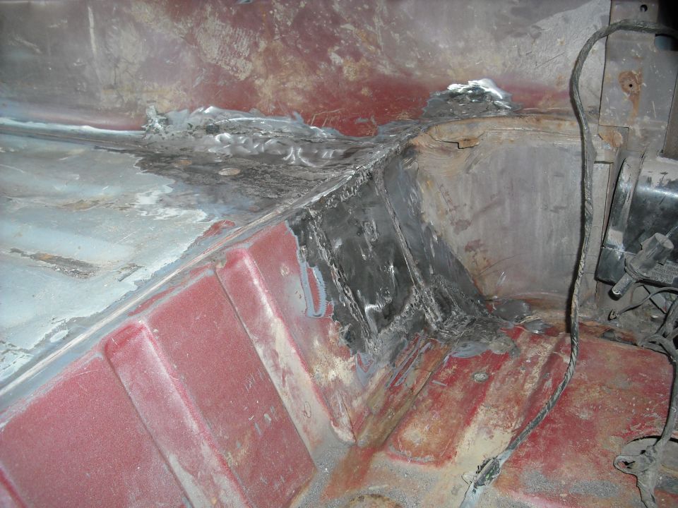 Fresh weld repair on a vehicle floor pan with surrounding red paint