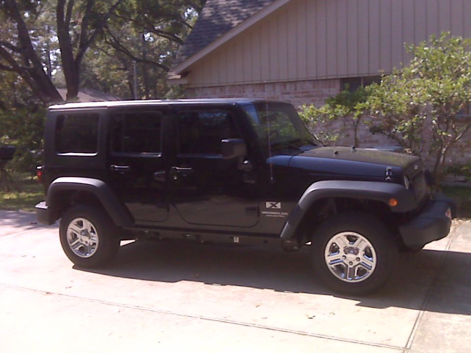 Black four-door Jeep Wrangler parked on a driveway, side view