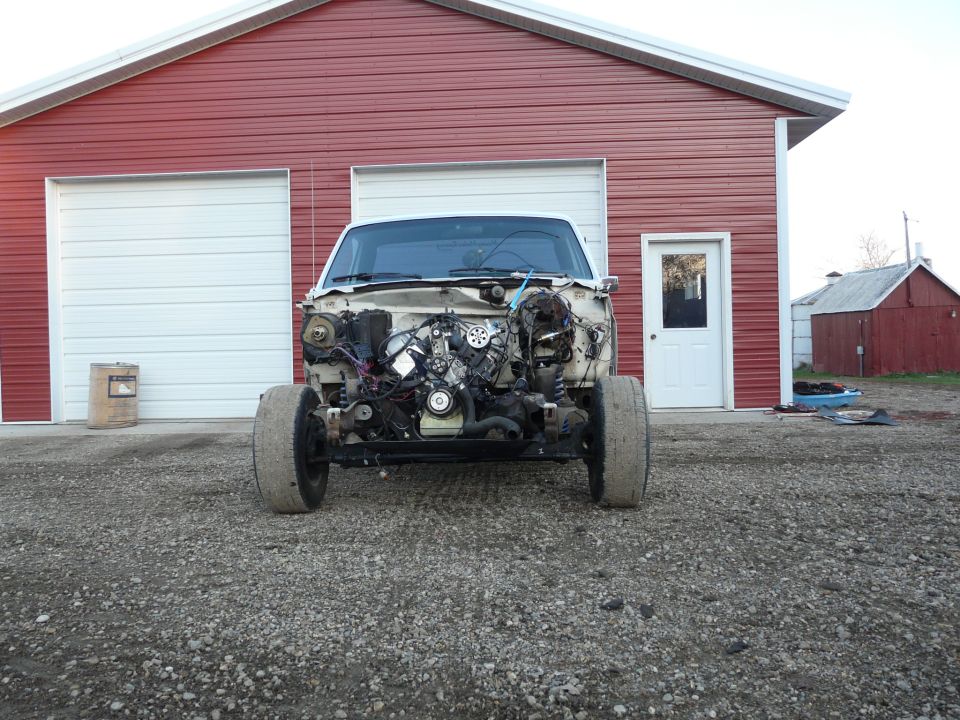 Stripped white pickup front end showing exposed engine, headers and wiring