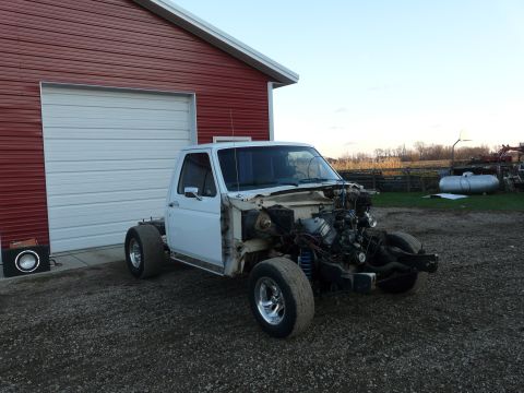 1994 Ford F-150 - Three-quarter front view of a white Ford pickup stripped to cab and frame on gravel next to a red barn, with the hood, fenders, grille and…