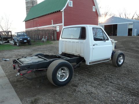 1994 Ford F-150 - Three-quarter rear view of a white Ford pickup cab on a bare rolling chassis outside a red gambrel-roof barn, with the bed and front clip r…