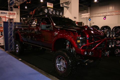 1998 Ford Crown Victoria - A heavily modified red pickup truck with custom paint and off-road modifications is displayed indoors.