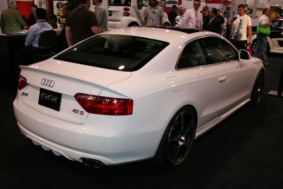 Rear 3/4 view of a white Audi A5 coupe with a spoiler and aftermarket wheels