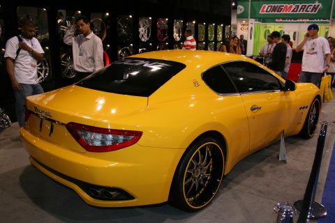 1998 Ford Crown Victoria - A yellow Maserati GranTurismo coupe is displayed indoors with people and car parts in the background.