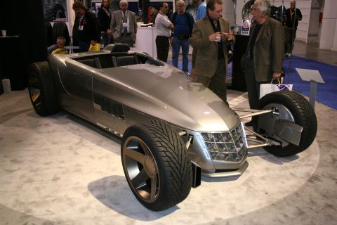 1998 Ford Crown Victoria - A unique silver concept car is displayed indoors with people observing.