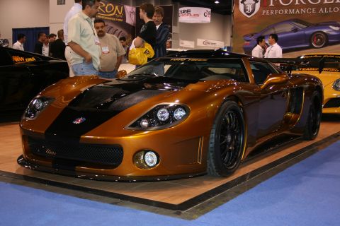 1998 Ford Crown Victoria - A custom sports car with a striking orange and black paint scheme is displayed at an auto show.