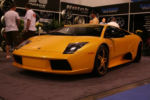 1998 Ford Crown Victoria - A bright yellow Lamborghini Gallardo is showcased at an event, custom wheels and a backdrop of automotive displays.