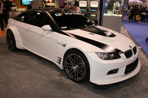 1998 Ford Crown Victoria - A modified white BMW M3 with black racing stripes and a widebody kit is displayed indoors.