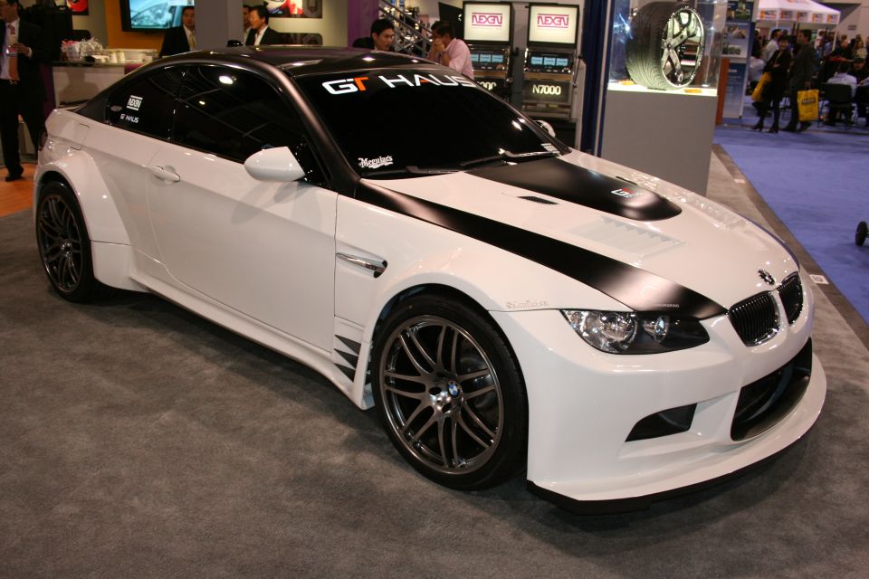 White BMW M3 with black racing stripes and widebody kit, parked indoors