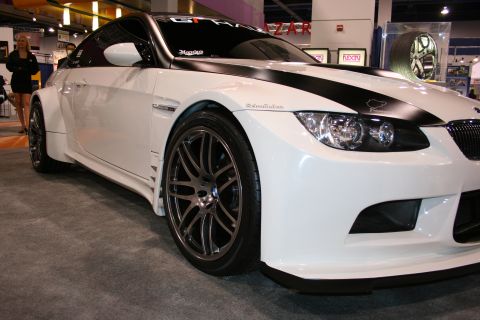 1998 Ford Crown Victoria - Customized white BMW M3 with a wide body kit and black racing stripes displayed at an auto show.