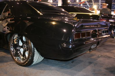 Rear quarter view of a black custom car with chrome wheels and a spoiler. Another black car is visible behind