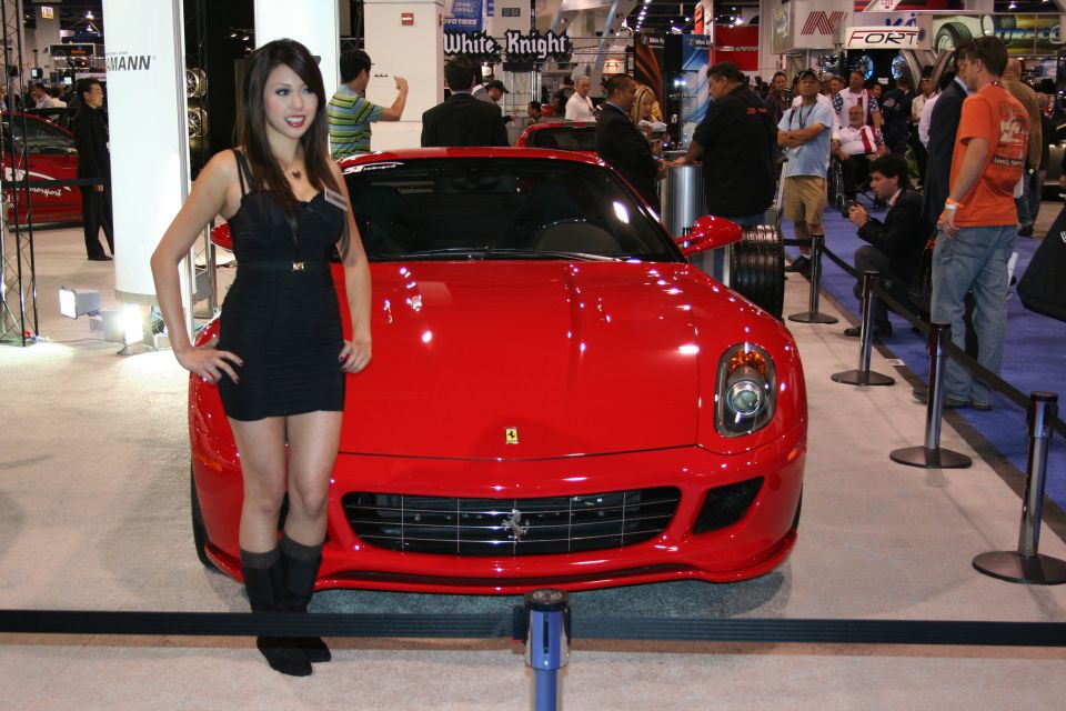 Woman in black dress next to a red Ferrari sports car at an auto show