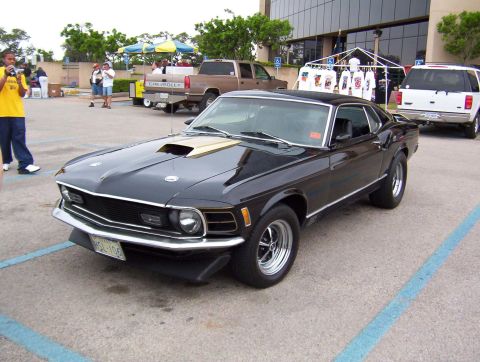 1970 Ford Mustang - A black 1970 Ford Mustang is parked in a lot with other vehicles and people in the background.