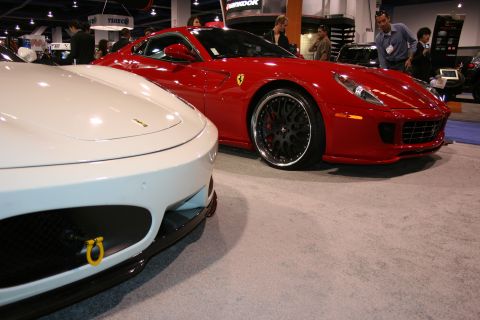 Front view of a white sports car next to a red Ferrari sports car at an auto show