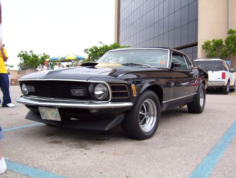 1970 Ford Mustang - This black 1970 Ford Mustang coupe features distinctive gold trim and a front 3/4 view, with a Texas license plate visible.