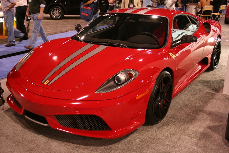 Red Ferrari sports car with silver racing stripes on the hood and roof, black wheels, and a yellow Ferrari emblem on the front fender