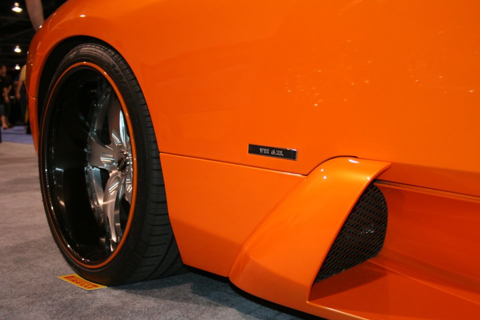 Close-up of an orange sports car's side, showing a custom wheel and a badge that reads "V10 5.2L"