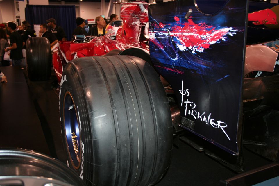 Close-up of a Formula 1 car's rear tire and sidepod with abstract art and a signature