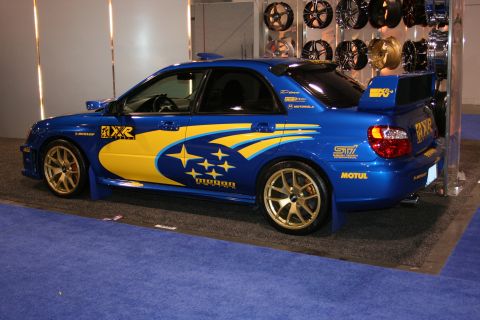 Blue Subaru WRX STI with yellow graphics and gold wheels, rear spoiler, and mud flaps