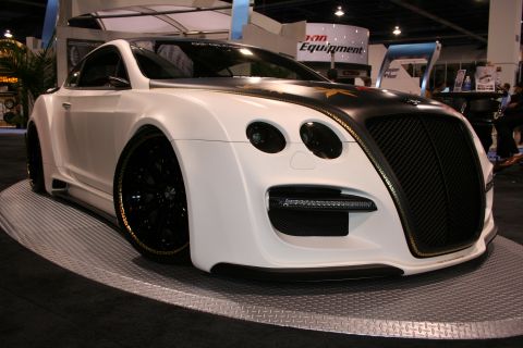 White custom coupe with black grille and gold trim, on display platform