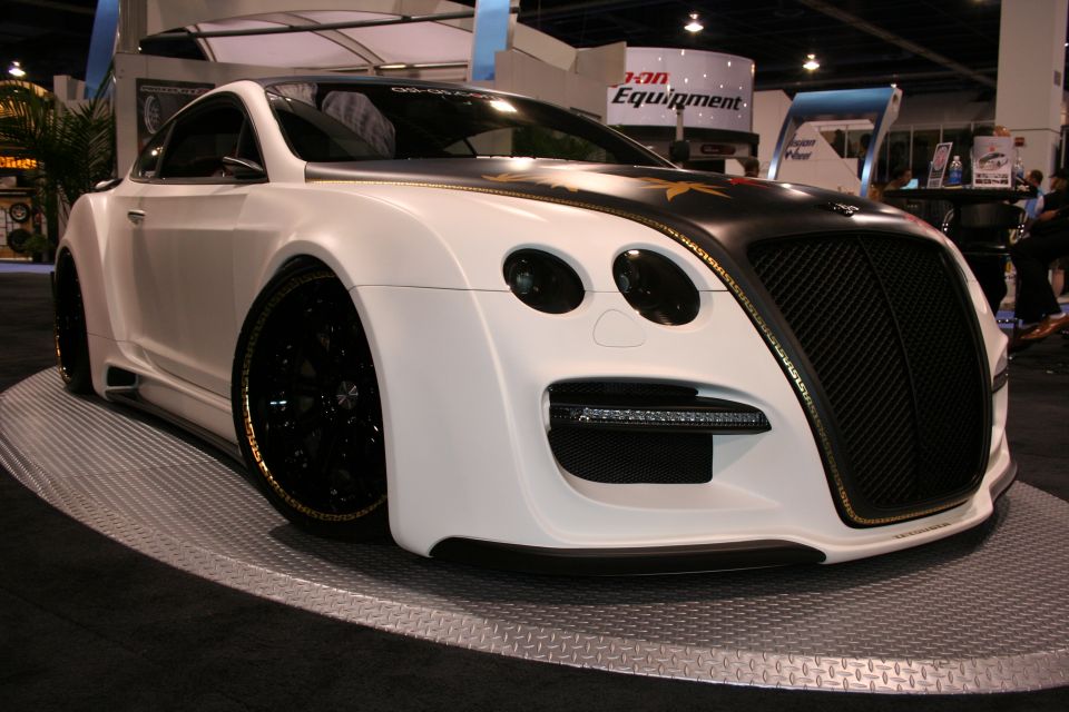 White custom coupe with black grille and gold trim, on display platform