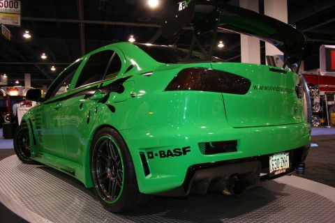 Green Mitsubishi Lancer Evolution with black racing stripes and a large rear spoiler, viewed from the rear-rig