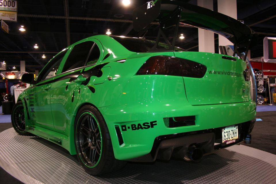 Green Mitsubishi Lancer Evolution with black racing stripes and a large rear spoiler, viewed from the rear-right