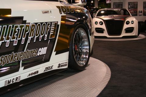 Close-up of a customized white car with 'BULLETPROOF AUTOMOTIVE' graphics, showing its side and wheel. Another