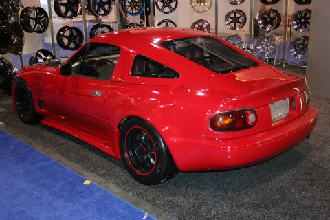 Red sports car with black wheels and red trim, rear 3/4 view, on display